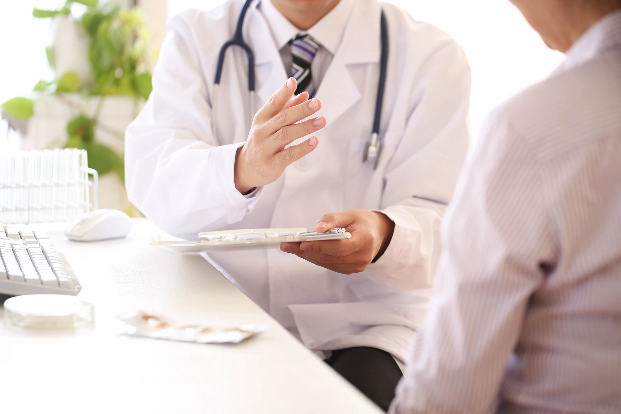 Doctor in a white coat consulting with a patient, holding a clipboard and gesturing during a medical discussion in a clinic